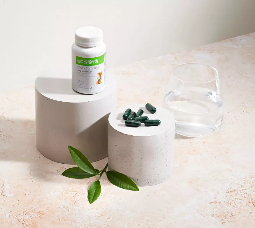 Herbalife Phyto Complete Supplement bottle, capsules, and a glass of water on a light surface with a leaf.