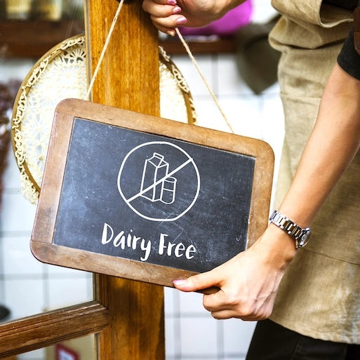 Person holding a chalkboard sign indicating 'Dairy Free' with a blurred background portraying Herbalife Dairy Free Products.