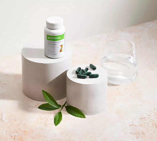 Herbalife Phyto Complete Supplement bottle, capsules, and a glass of water on a light surface with a leaf.