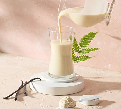 Glass of Herbalife Vegan Protein Drink being poured with a vanilla bean and powder on a light pink background