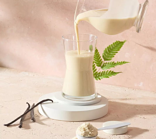 Glass of Herbalife Vegan Protein Drink being poured with a vanilla bean and powder on a light pink background